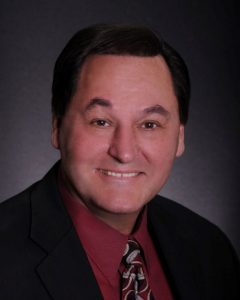 A person in a suit smiling Description automatically generated